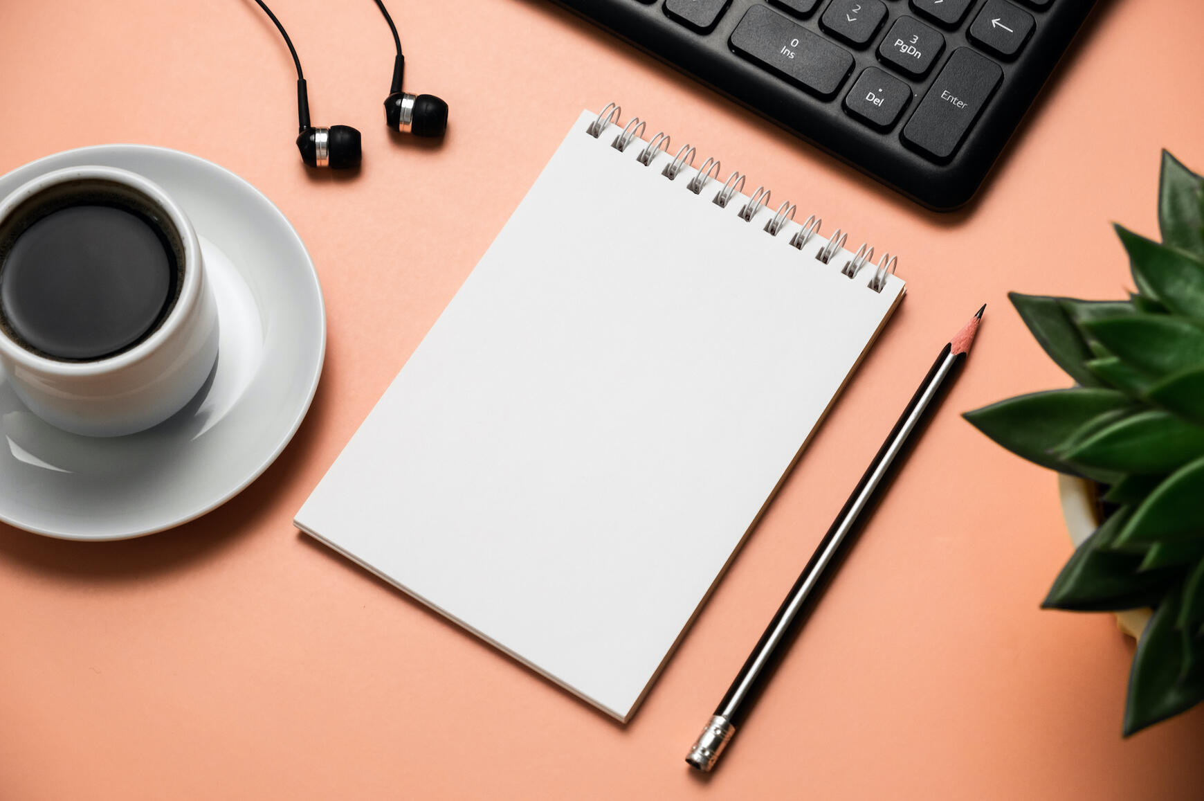 Coral desk flatlay with notepad, coffee, headphones, and keyboard, representing virtual assistant contact and business support.